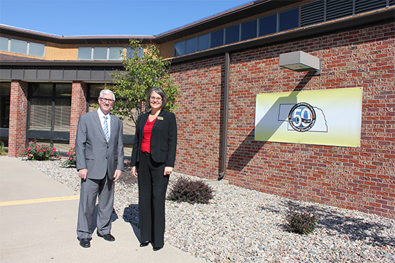 Treasurer Stenberg with Larianne Polk outside ESU7 offices in Columbus. A nearby poster celebrates the 50th anniversary of ESUs in Nebraska.